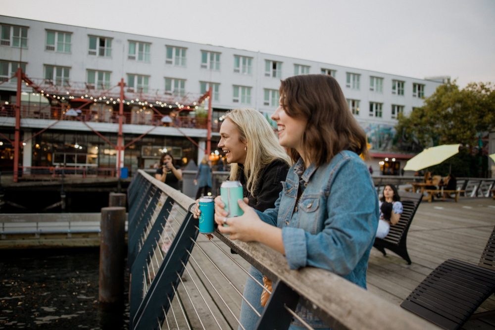 Two women drinking beer from cans on pier