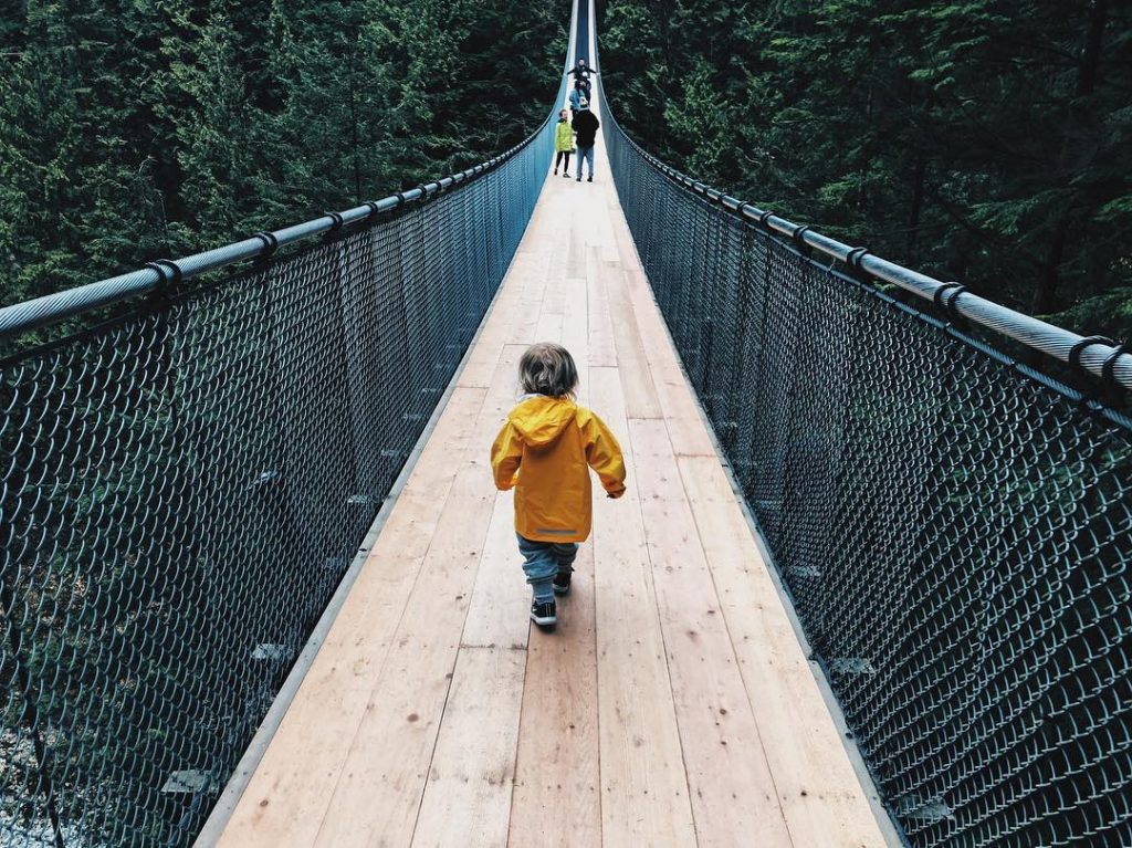child in raincoat running along suspension bridge